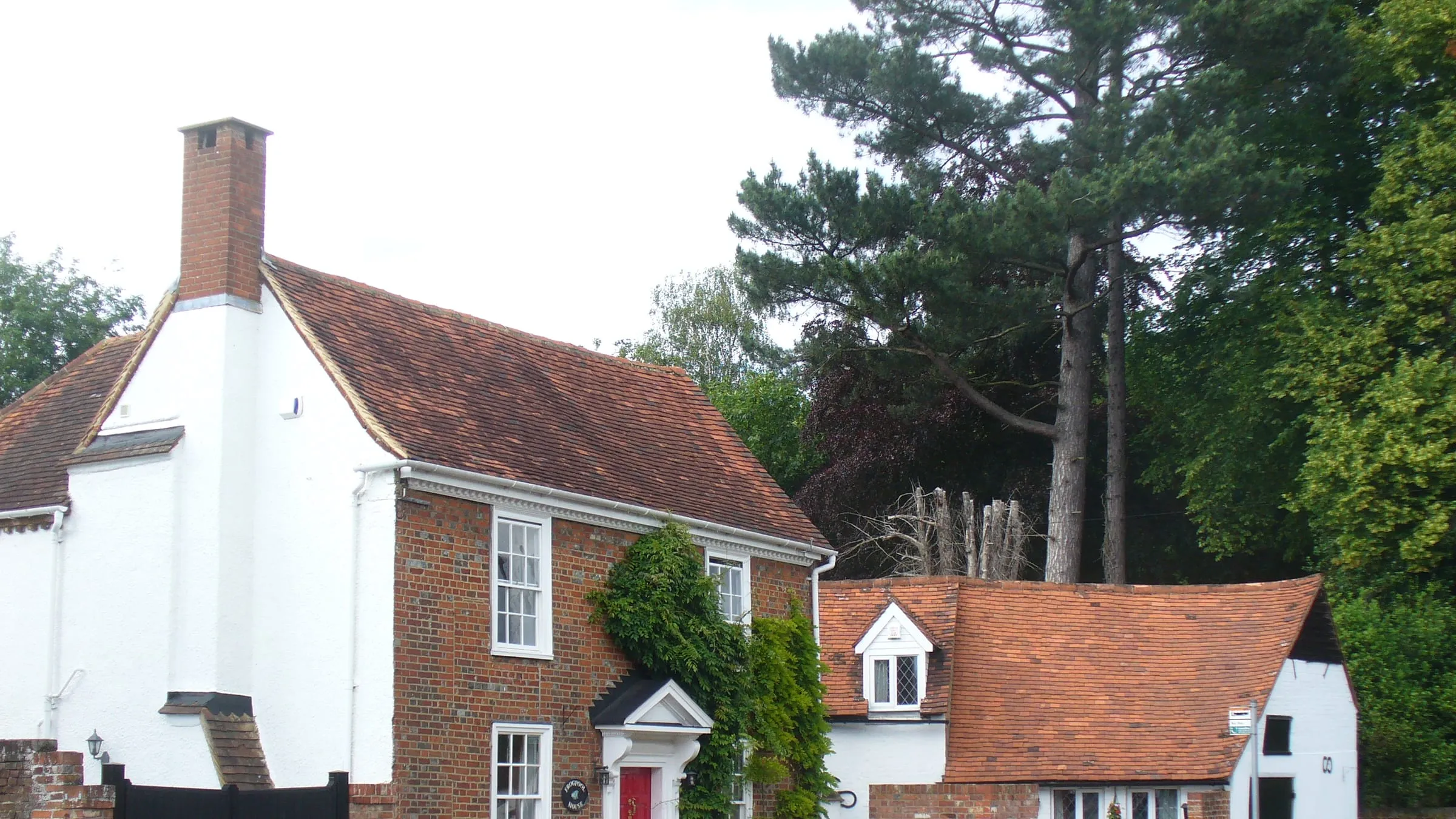 Old brick and white-painted houses in the centre of Chobham village, under tall pines