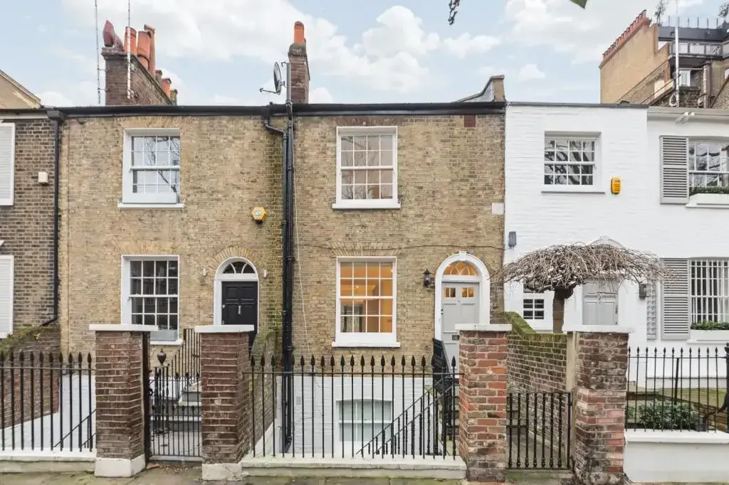 The front of a pair of Georgian brick terraced houses with sash windows, arched doorways and iron railings.