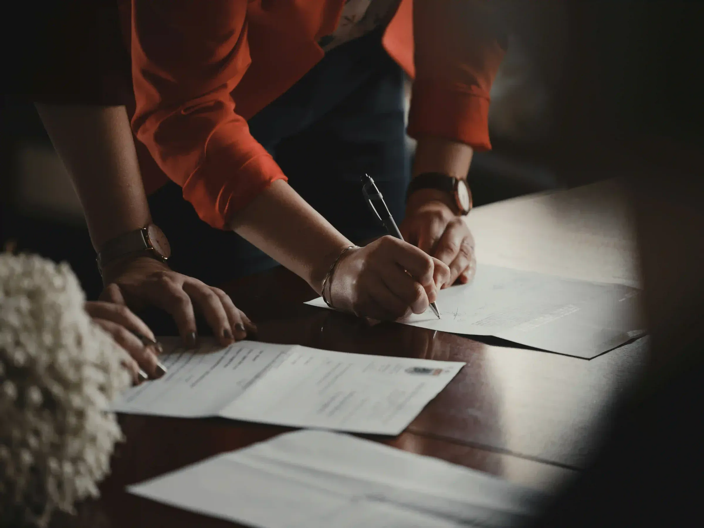 Two people at a table, one signing a document.