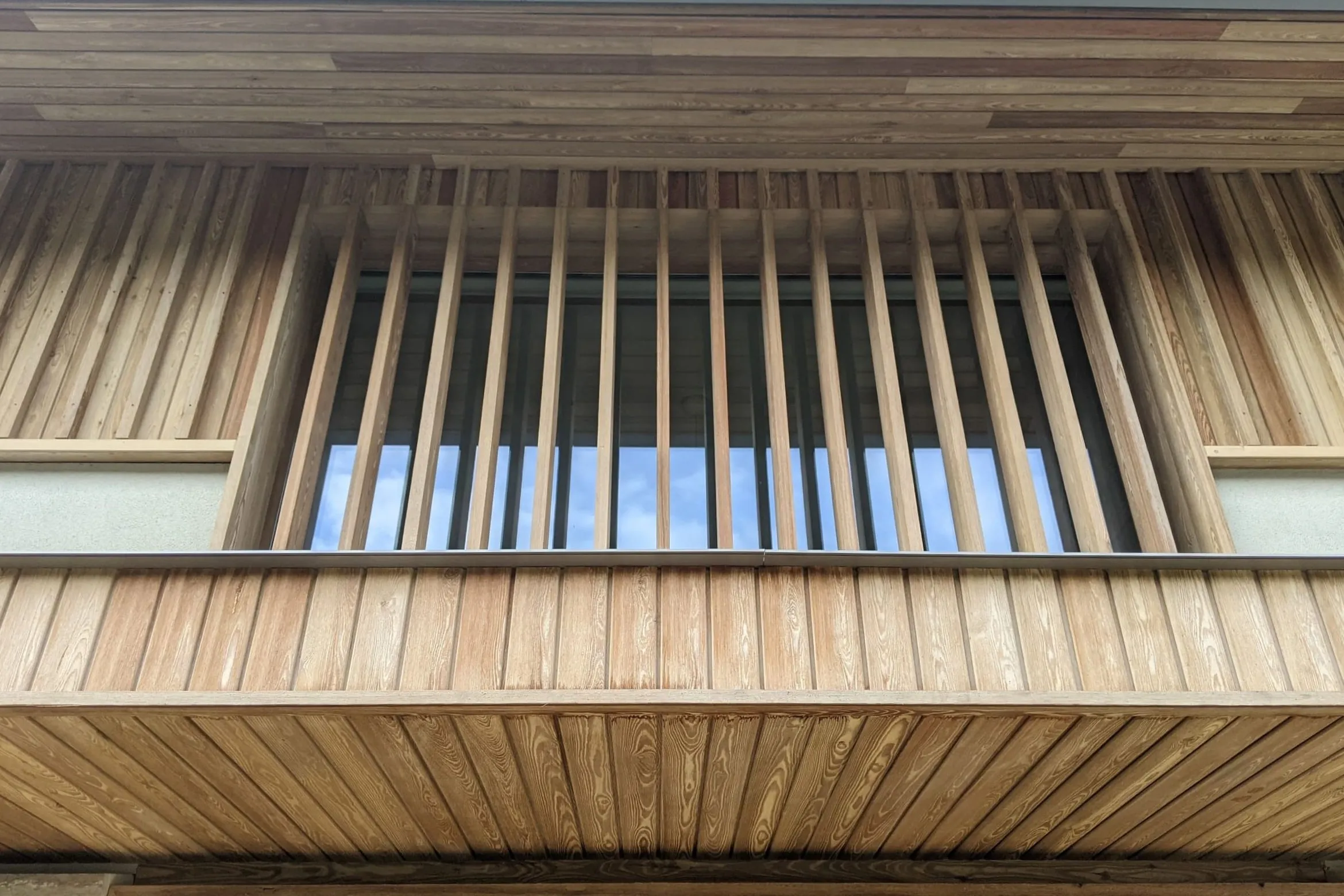The timber fin screen over the entrance, seen from below, with the larch soffit and cladding around it