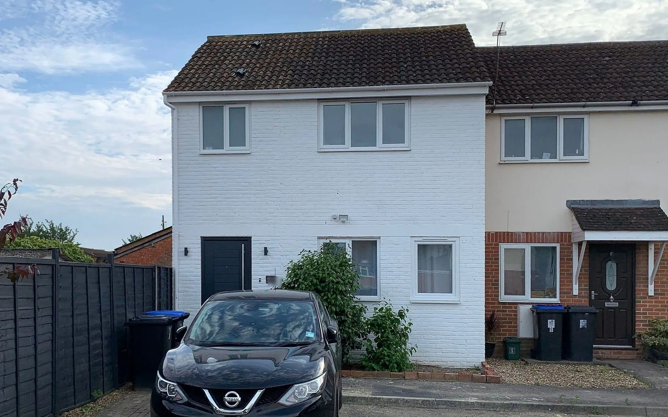 The extended end-of-terrace house in Woking, painted white, with the new two-storey side extension beside the original house and a car on the drive