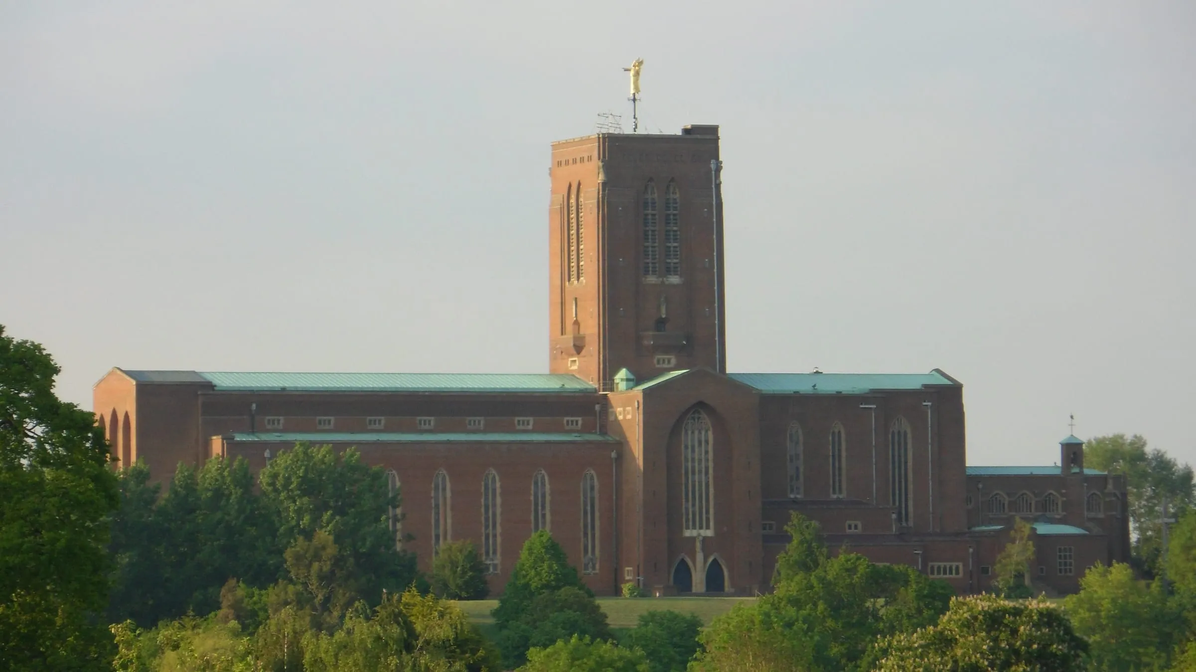 Guildford Cathedral in red brick on Stag Hill, seen above trees from Onslow Village