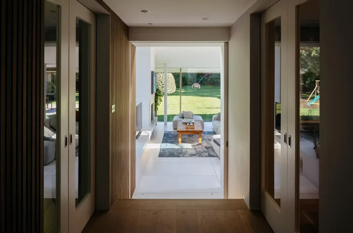 A view down a hallway with timber-slatted walls into a bright living room that opens onto the garden.