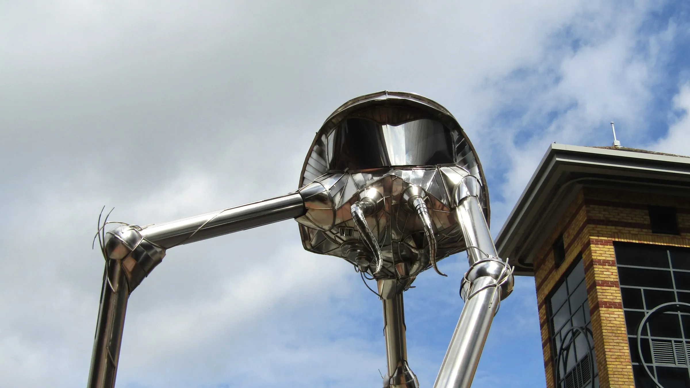 The stainless steel Martian sculpture in Woking town centre, its tripod legs against a cloudy sky