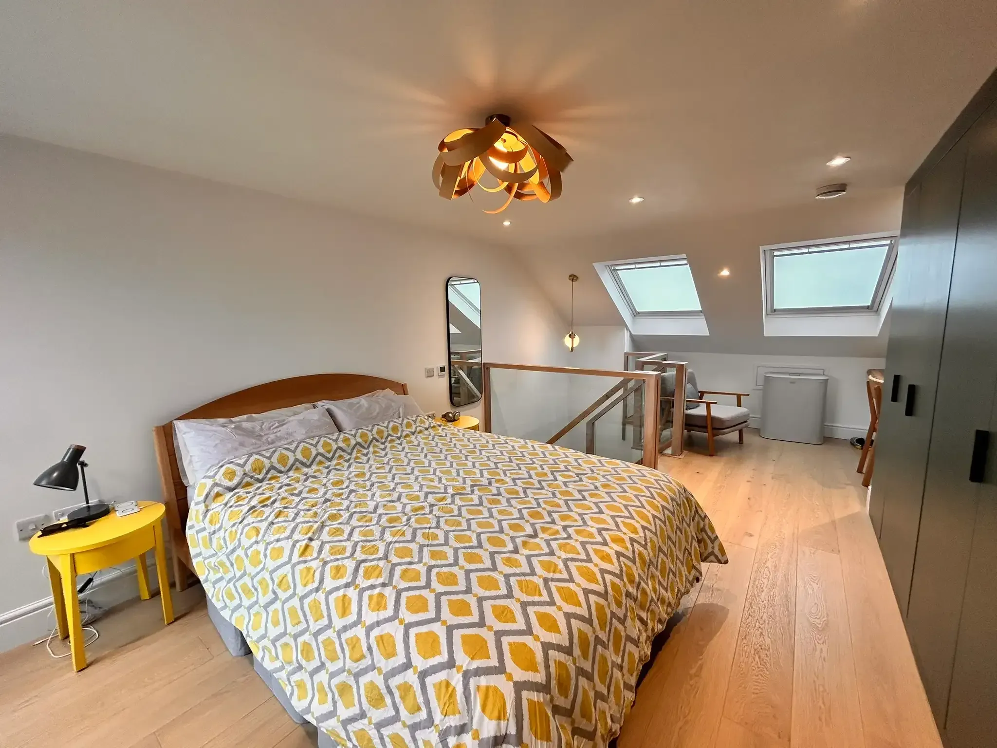 A loft conversion bedroom with oak flooring, two rooflights, yellow patterned bedding and dark grey built-in wardrobes.