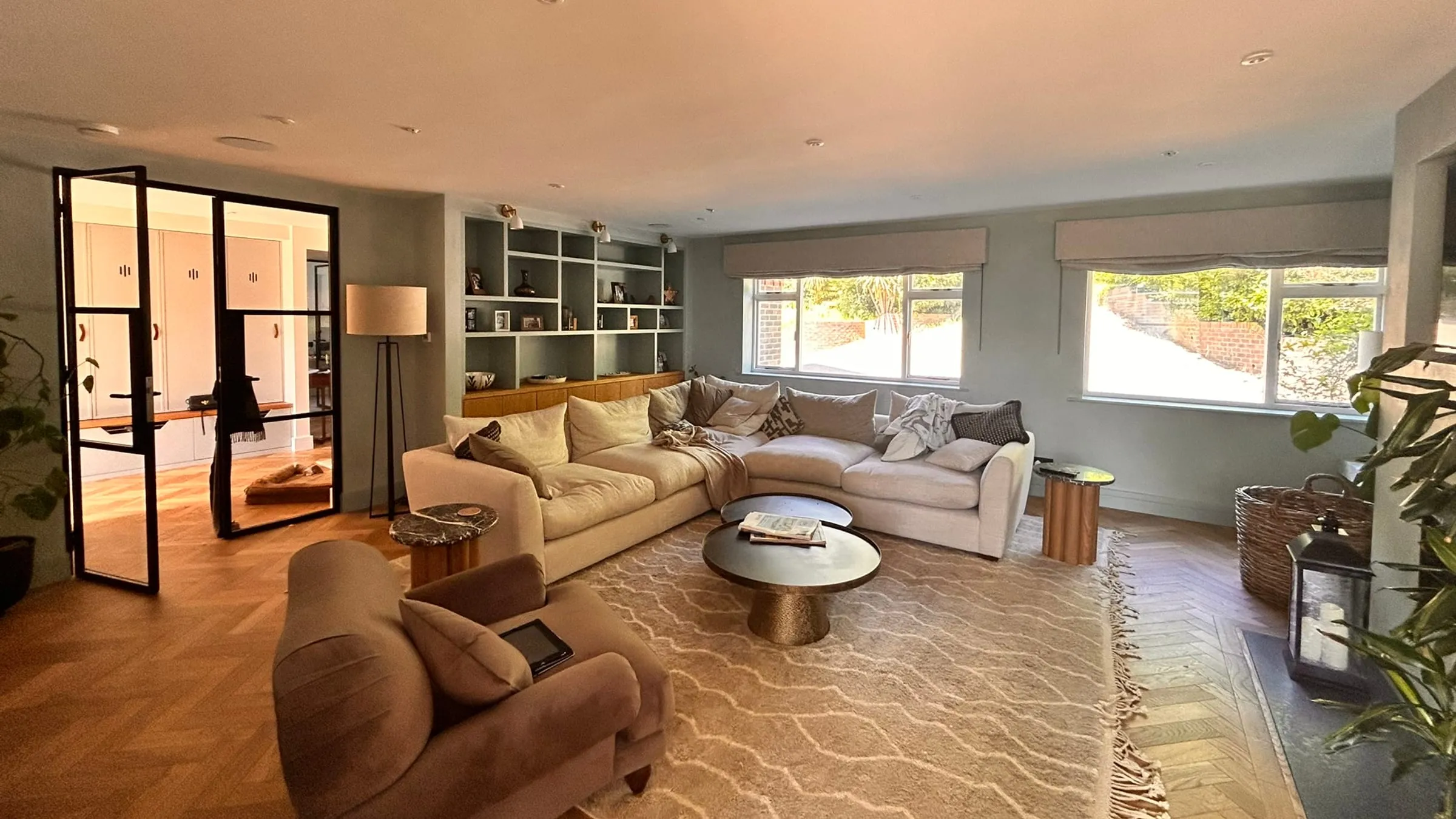 A long, light living room with a corner sofa, steel-framed glazed doors and built-in shelves