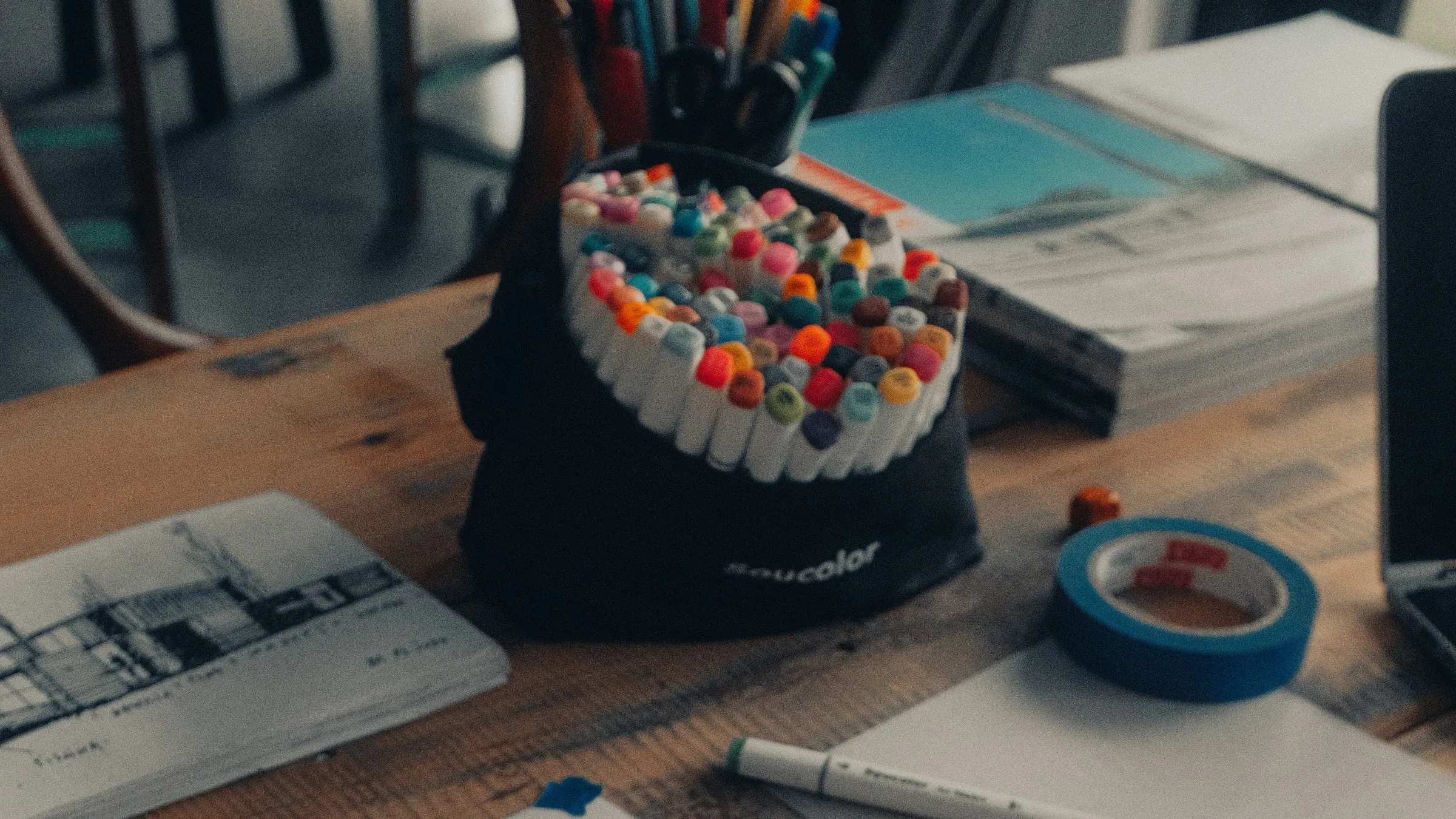An architect's desk with a pot of marker pens, sketchbooks of house drawings and a roll of masking tape