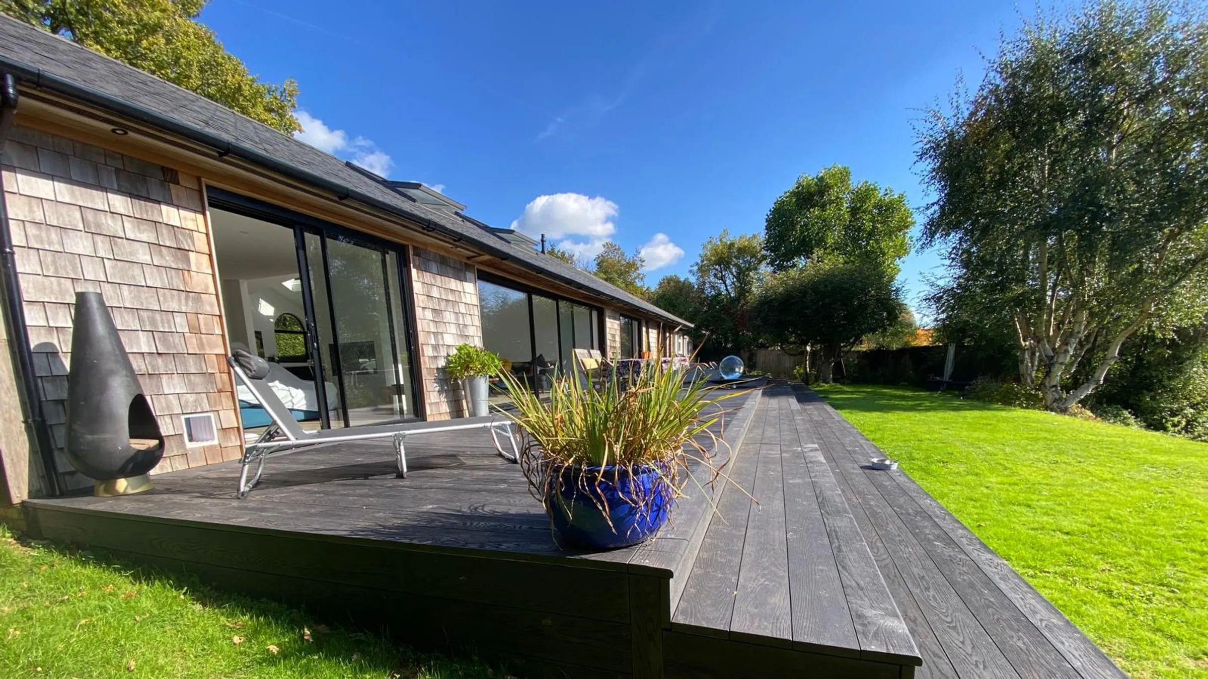 A single-storey house clad in cedar shingles, with a long timber deck and sliding glass doors onto a lawn