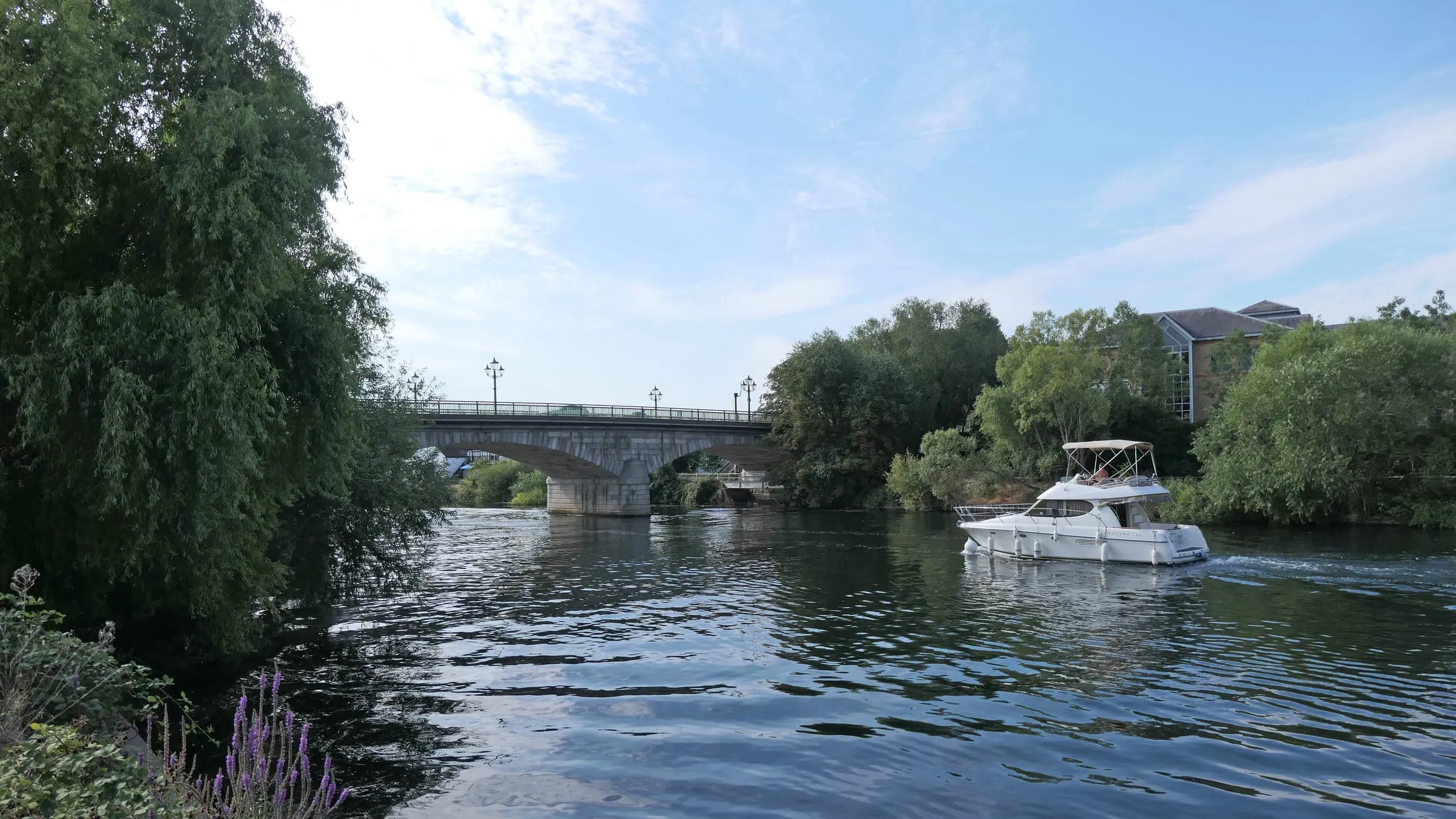 A cruiser on the River Thames at Staines, with Staines Bridge and willows beyond