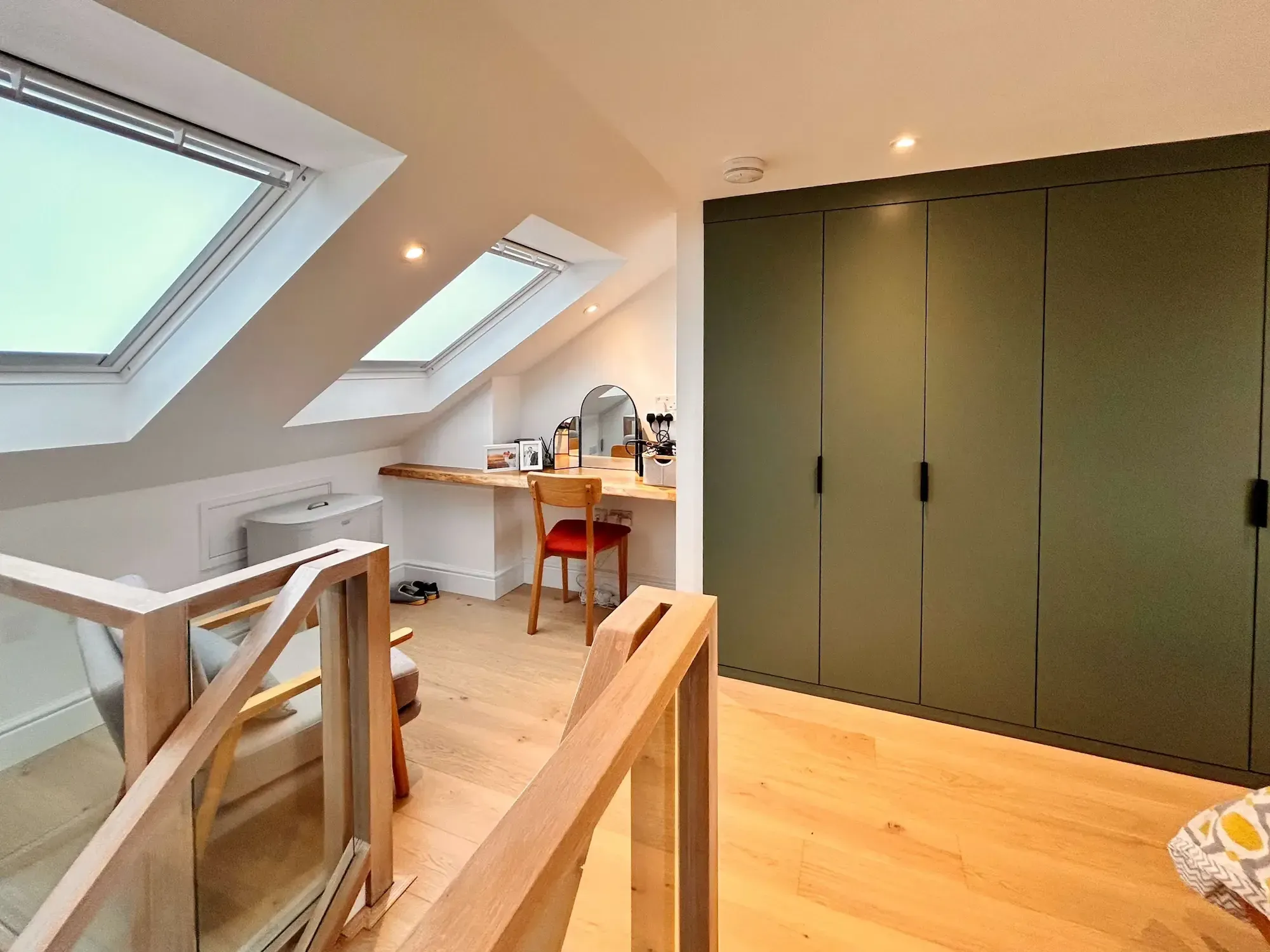 A converted loft room with two rooflights, a desk under the slope, green built-in wardrobes and an oak stair balustrade.