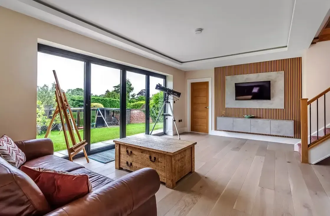 A living room with a leather sofa, a timber chest, slatted wall panelling and wide glazed doors onto a garden.