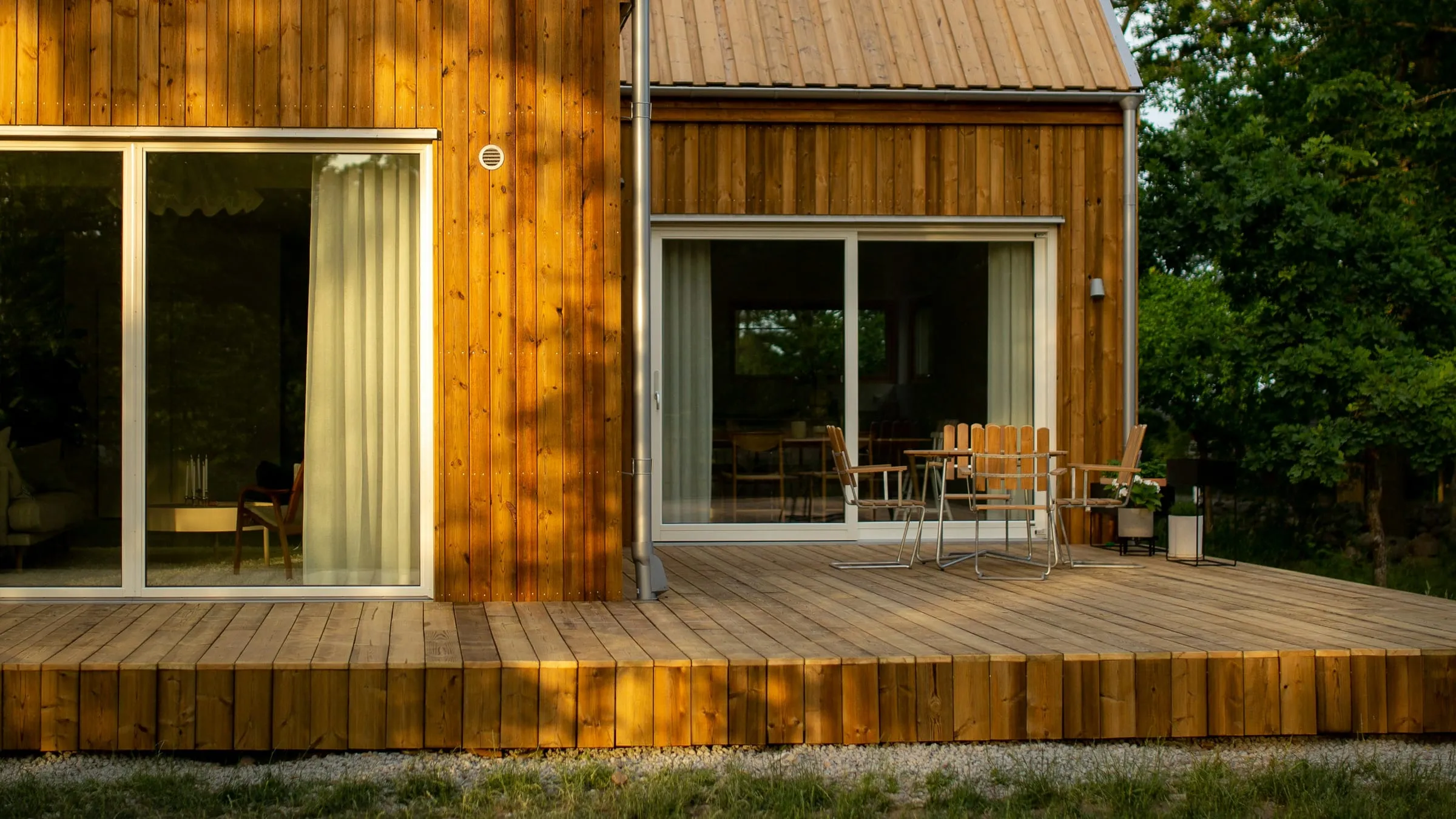 A timber-clad house with large sliding glass doors opening onto a deck among trees