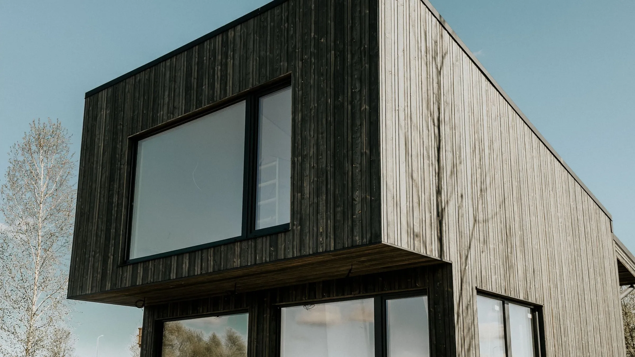A contemporary house clad in charred and natural timber, with a cantilevered upper floor and large picture windows.