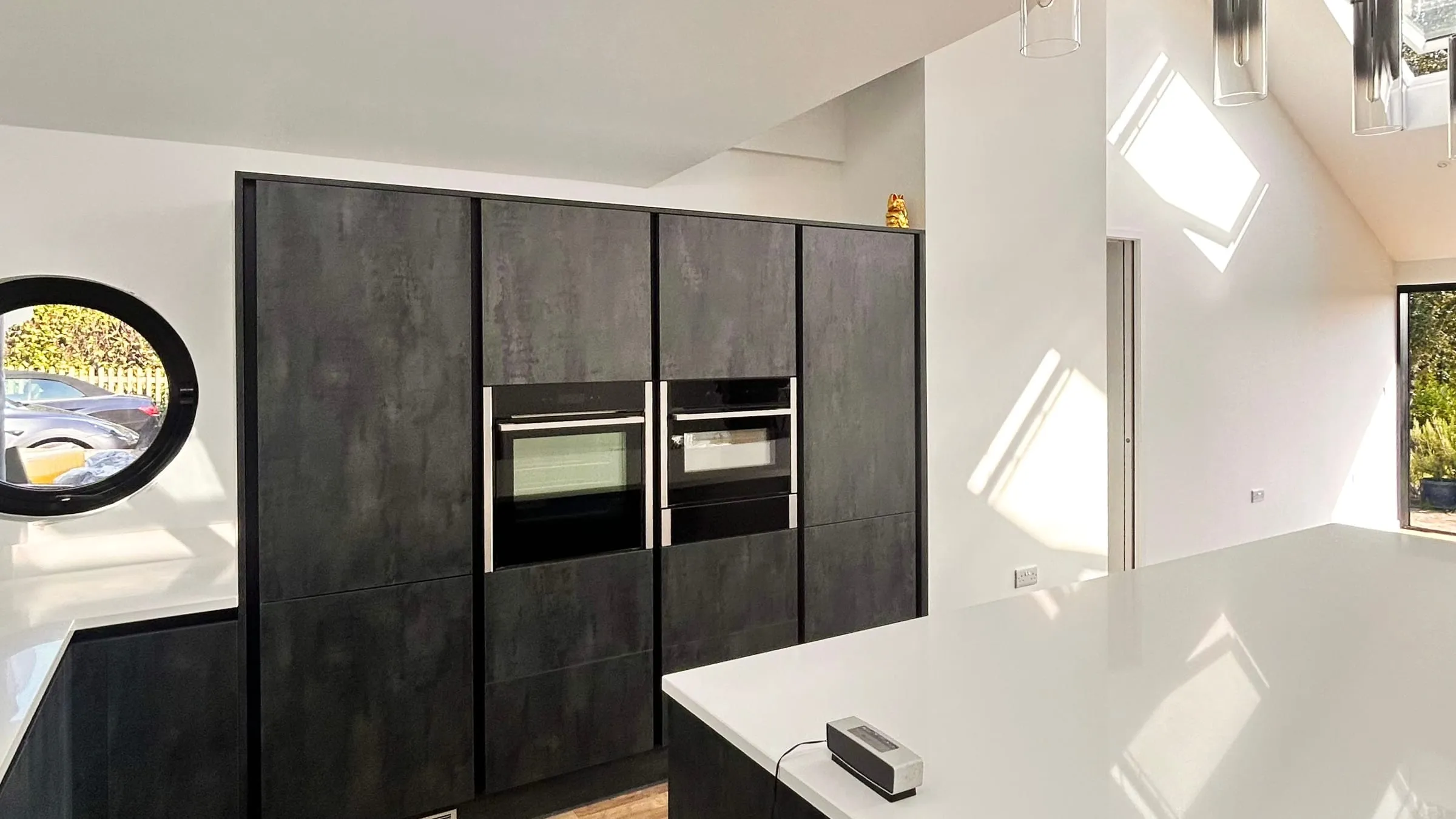 A vaulted kitchen extension with a white island, dark tall units, rooflights and a round window