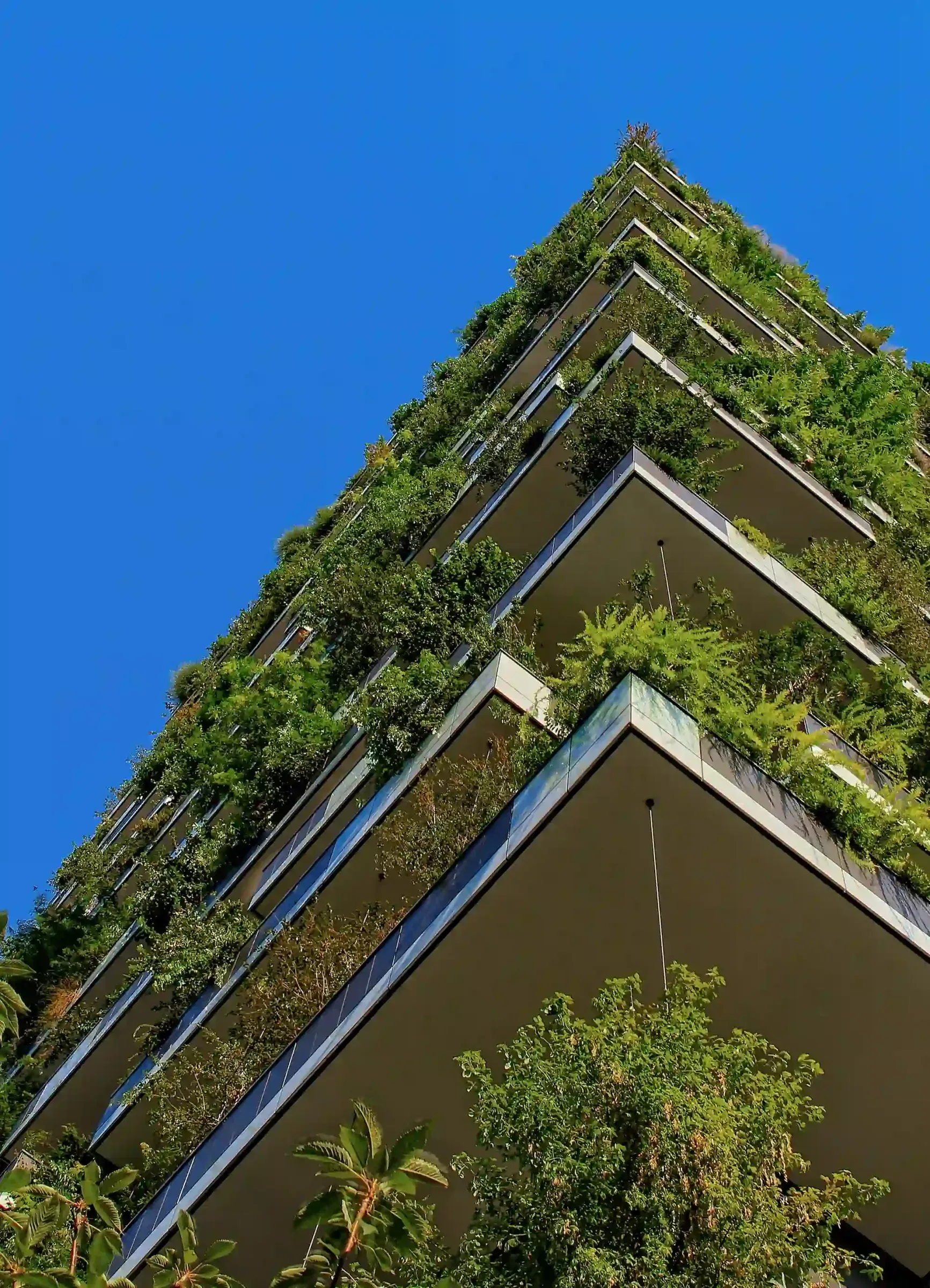 Looking up at a tall apartment building with trees and planting on every balcony.