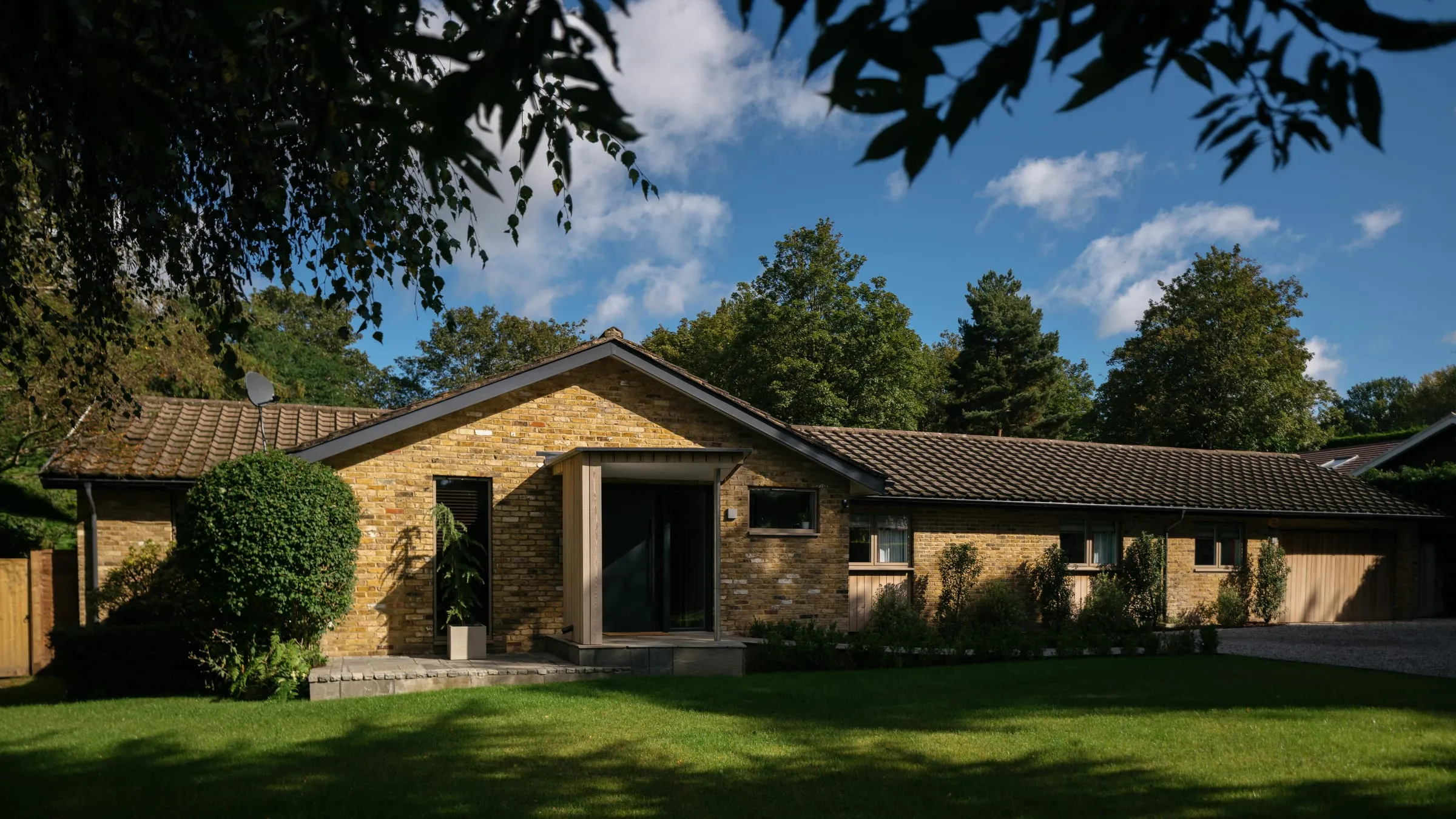 The front of a remodelled 1960s bungalow in Woking, with brick walls, a new roof and a mature garden