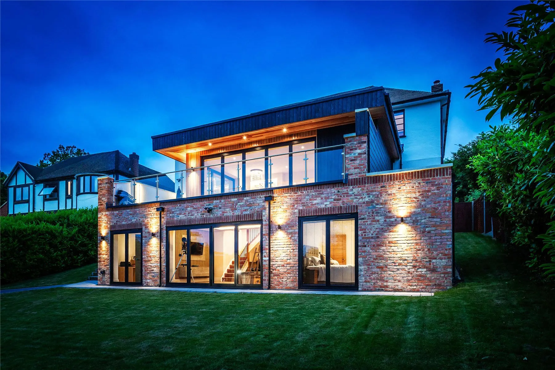 The garden side of the renovated Hook Heath house at dusk, with a new lower ground floor opening onto the lawn