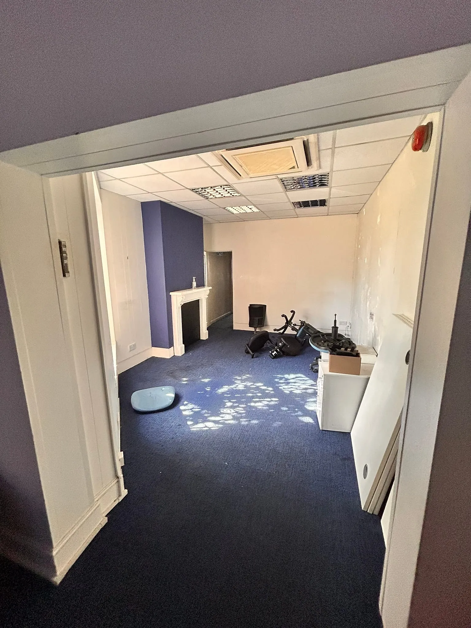 One of the office rooms before work, with a blocked fireplace, a suspended ceiling and a window at the far end