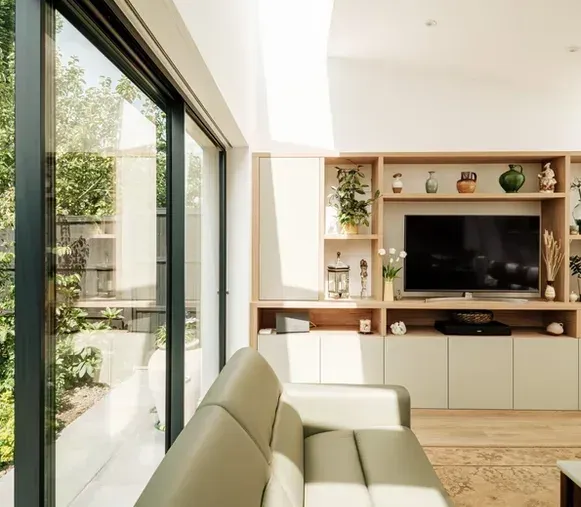 A living room with built-in timber shelving and sliding glass doors onto a garden.