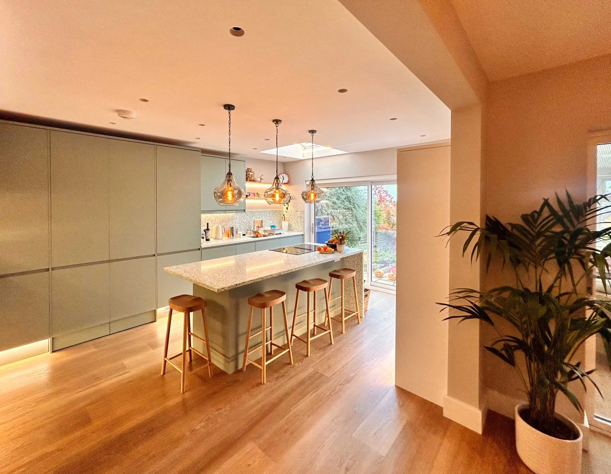 A long replanned kitchen in a Guildford house, with sage green units, an island and doors onto the garden