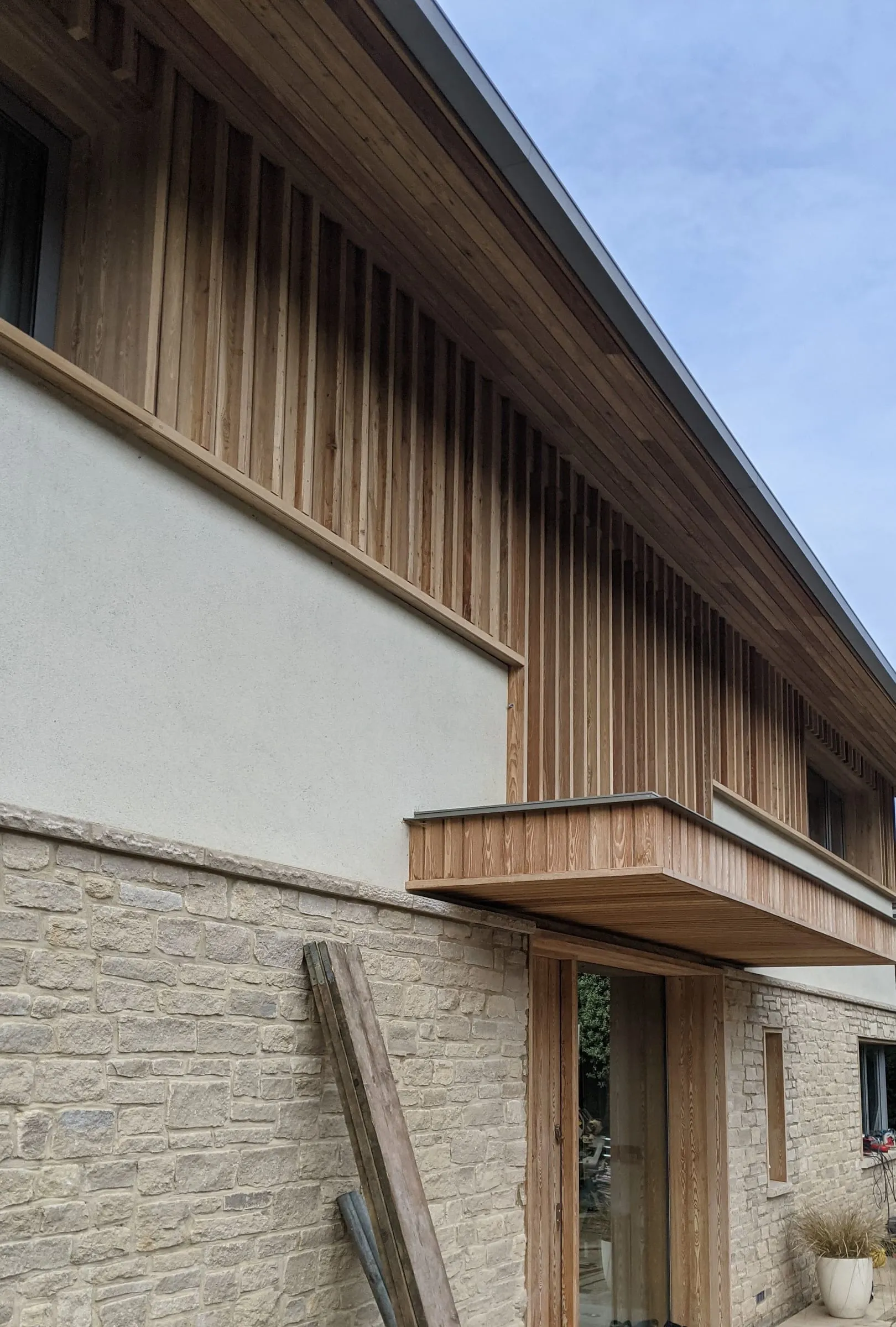 The side of the house, with the stone plinth, rendered walls and larch cladding above