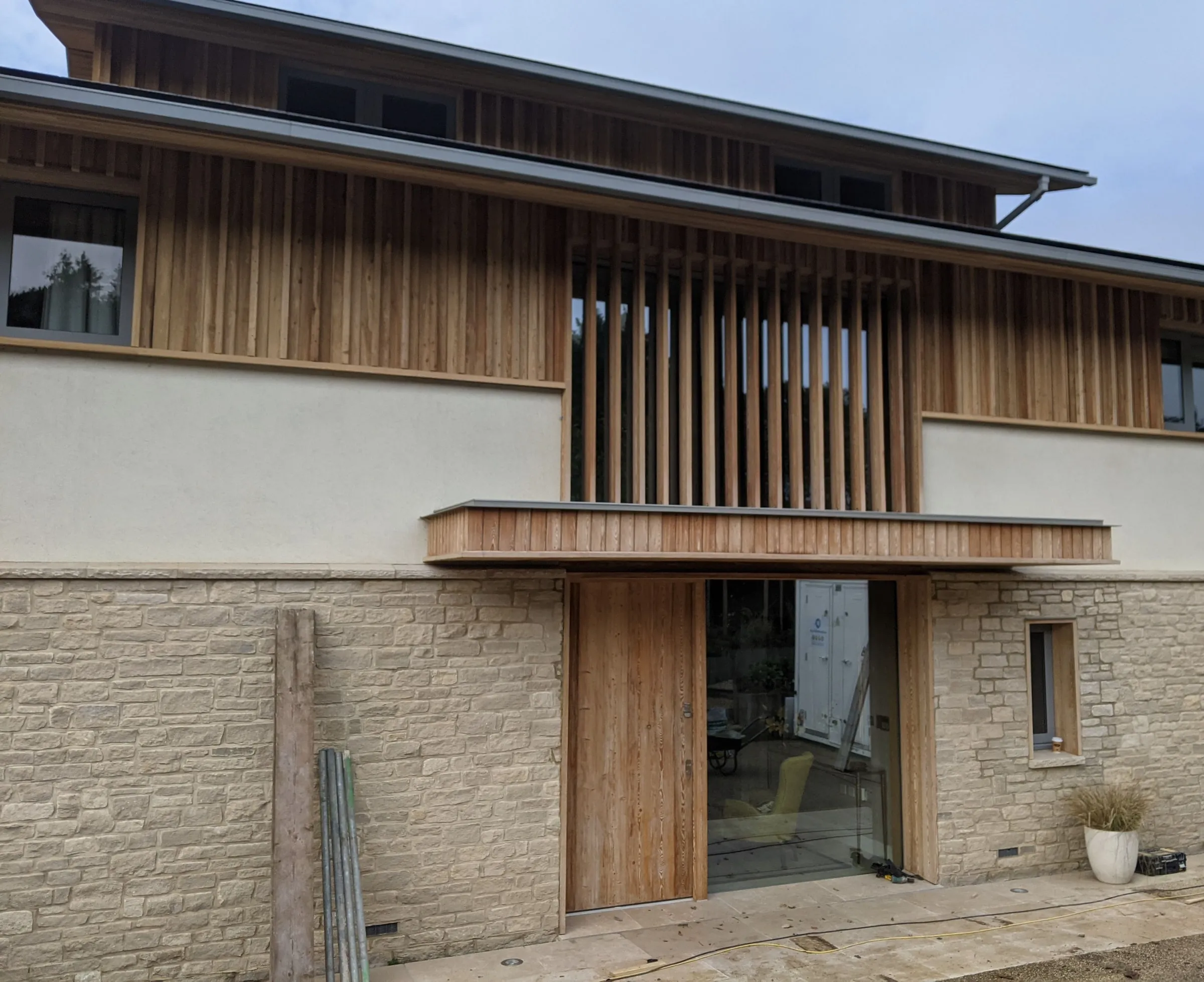 The entrance elevation during construction, the oak door and canopy under the timber fin screen, with the builder's ladders and planks still about