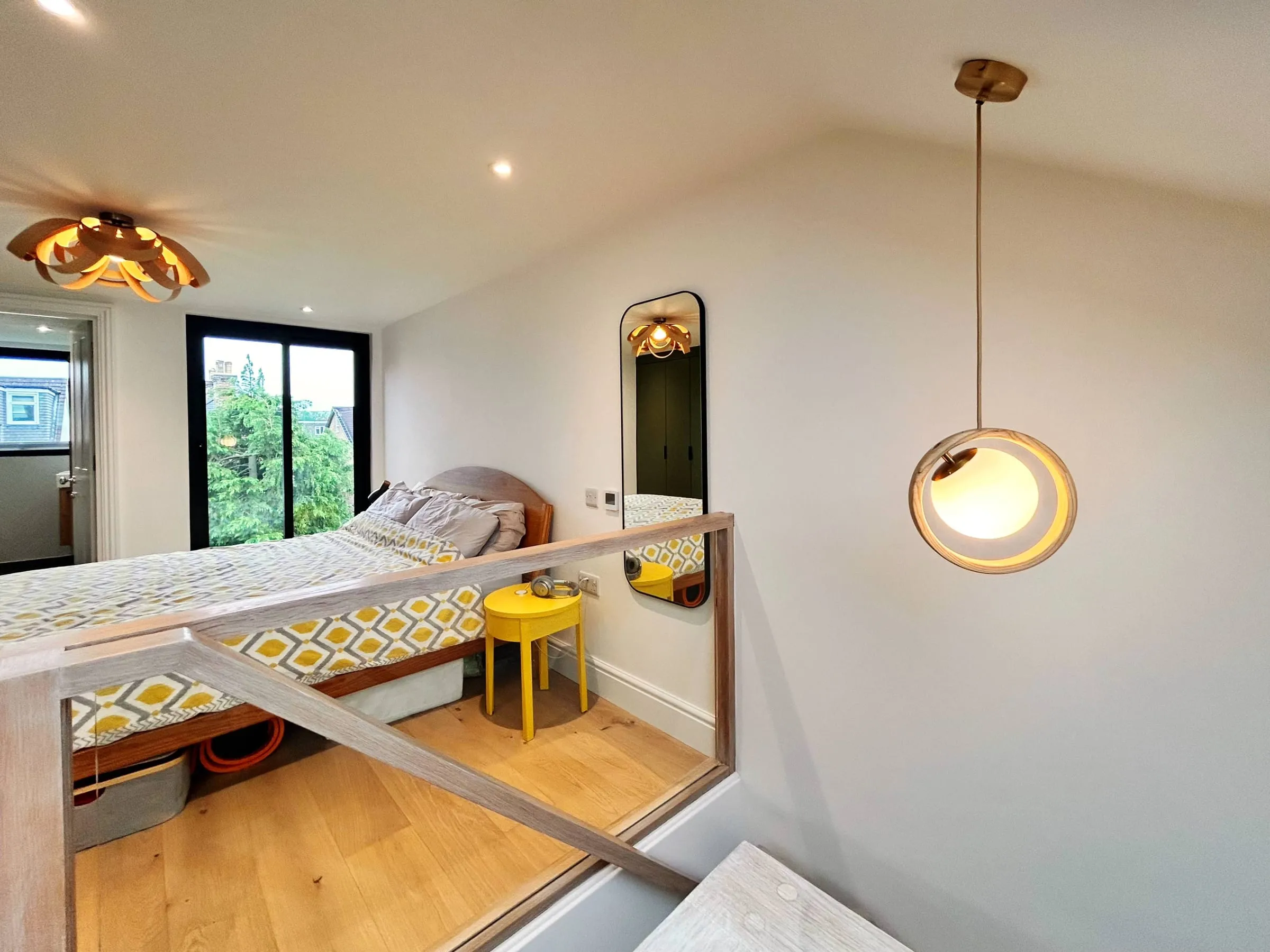A converted loft bedroom in a Guildford townhouse, with a sloping ceiling, a pendant light and a tall window