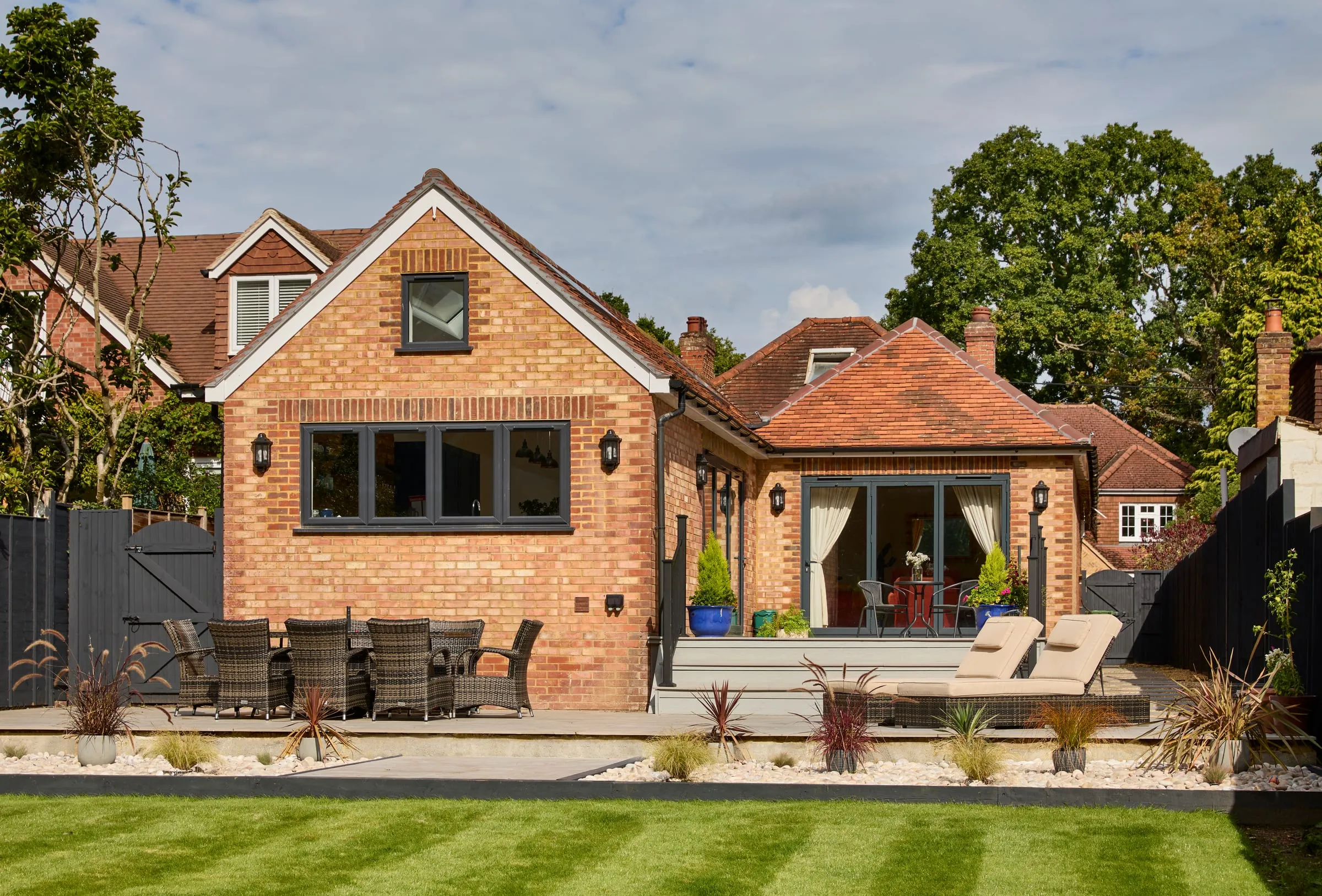 The rear of a brick house with a single-storey extension, folding doors onto a raised deck and a lawn in front.