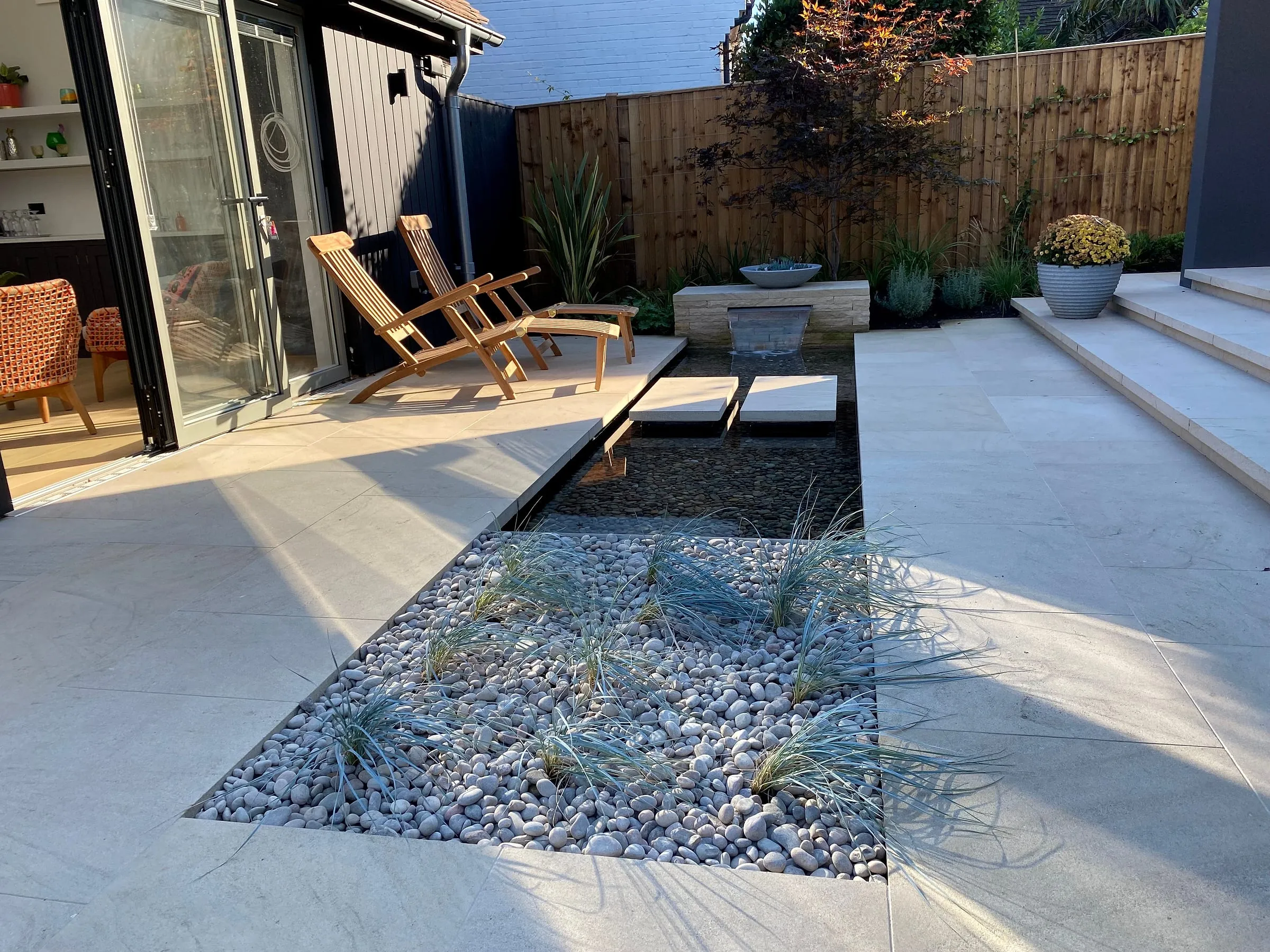 The stone terrace with a pond, deck chairs and the black-clad house